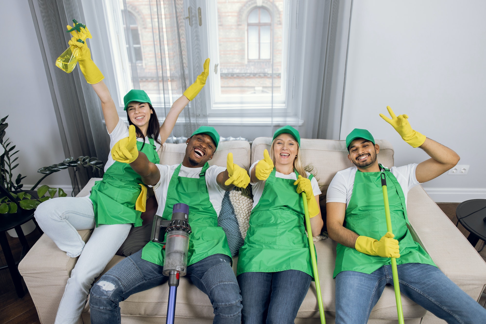 Team of housekeepers sitting on couch and showing thumb up