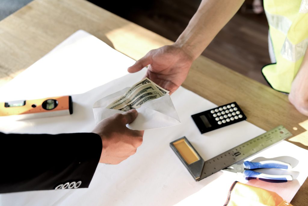 Top view of owner hand giving money to employee or hired person for his wage or salary over table.