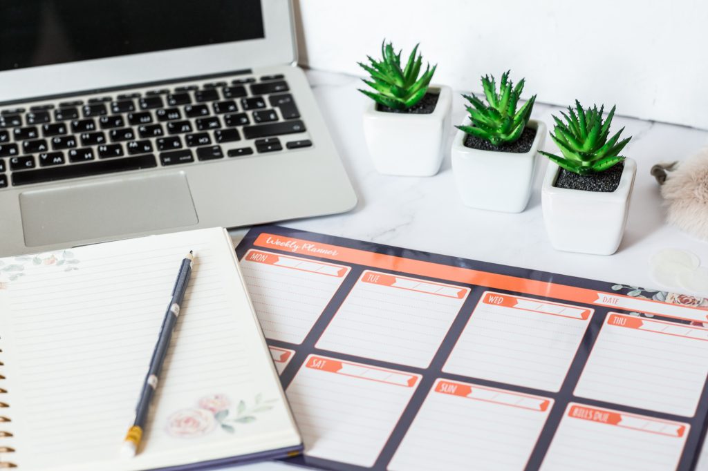 Working desk with weekly planner, notebook, succulent plants, laptop